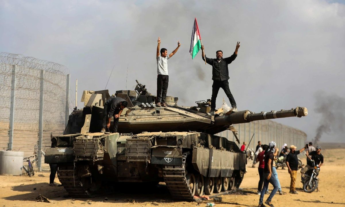 Palestinians celebrate on top of a destroyed Israeli tank on the Gaza border on 7 October.